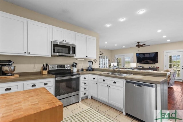 kitchen with ceiling fan, a sink, butcher block countertops, stainless steel appliances, and a peninsula