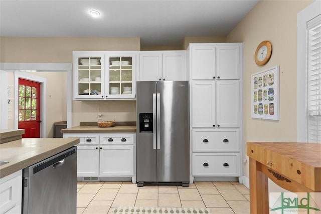 kitchen with stainless steel appliances, white cabinets, light tile patterned flooring, and glass insert cabinets