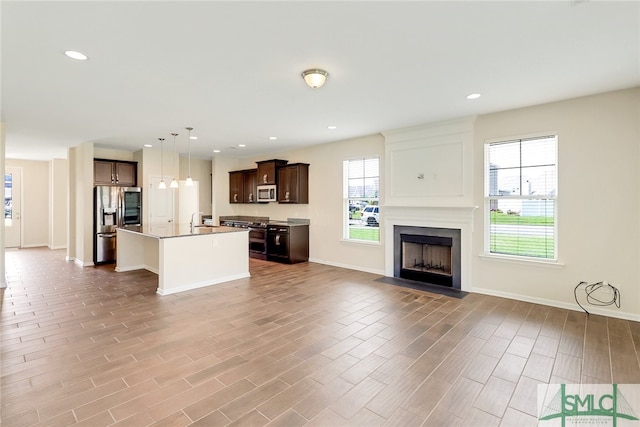 unfurnished living room featuring a sink, wood finished floors, baseboards, recessed lighting, and a fireplace with flush hearth