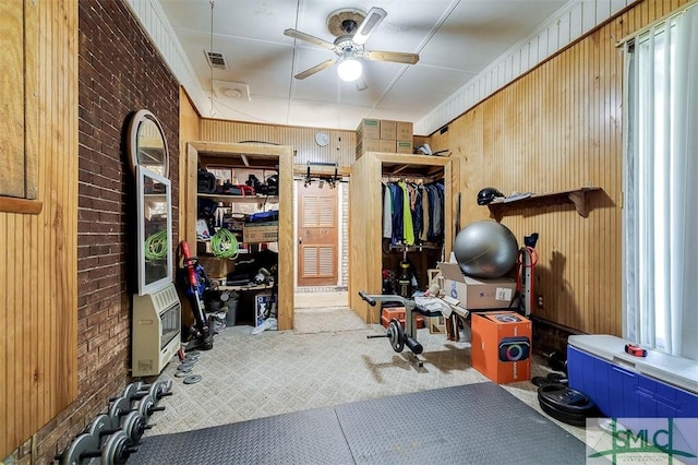 exercise room with ceiling fan, wood walls, heating unit, and visible vents