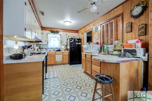 kitchen with ceiling fan, light countertops, white microwave, black refrigerator with ice dispenser, and under cabinet range hood