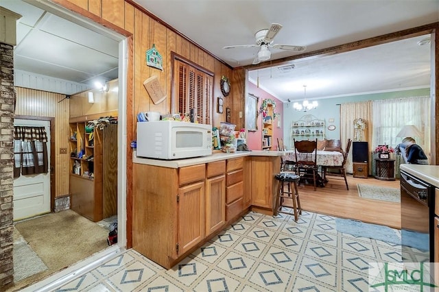 kitchen with wood walls, ornamental molding, ceiling fan with notable chandelier, and white microwave