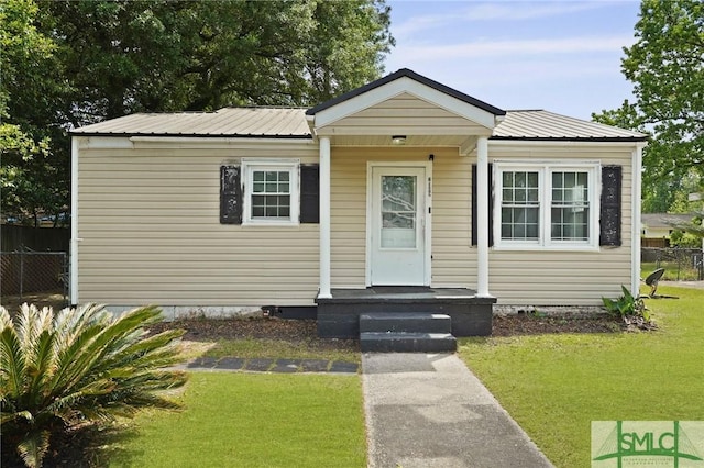 bungalow-style home with fence, metal roof, and a front lawn