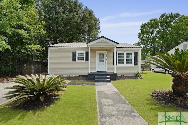 bungalow-style home featuring fence, metal roof, and a front lawn