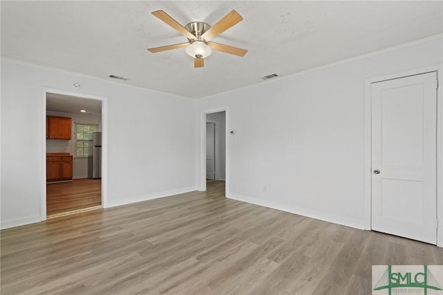 empty room featuring crown molding, ceiling fan, light wood-type flooring, and visible vents