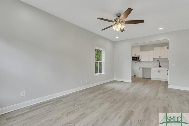 unfurnished living room with a sink, light wood finished floors, a ceiling fan, baseboards, and recessed lighting