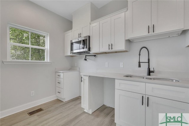 kitchen featuring visible vents, light wood-type flooring, light countertops, stainless steel microwave, and a sink