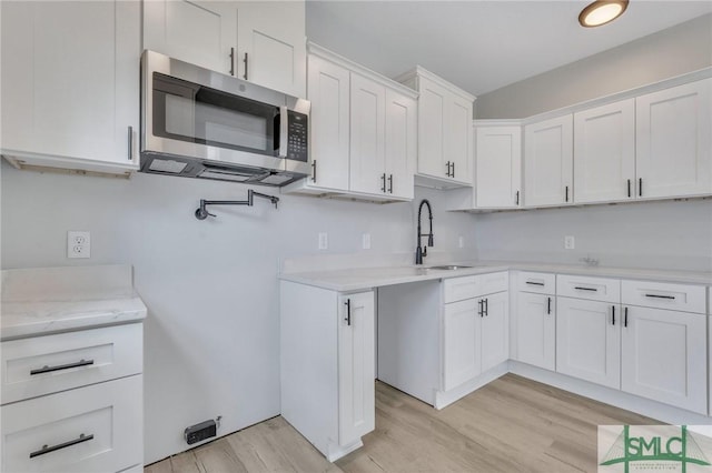 kitchen with light wood-style floors, a sink, stainless steel microwave, and white cabinets