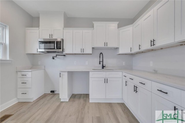kitchen with stainless steel microwave, visible vents, a sink, and light wood-style floors