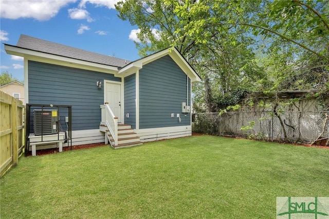 back of house featuring a fenced backyard, a yard, a shingled roof, and entry steps