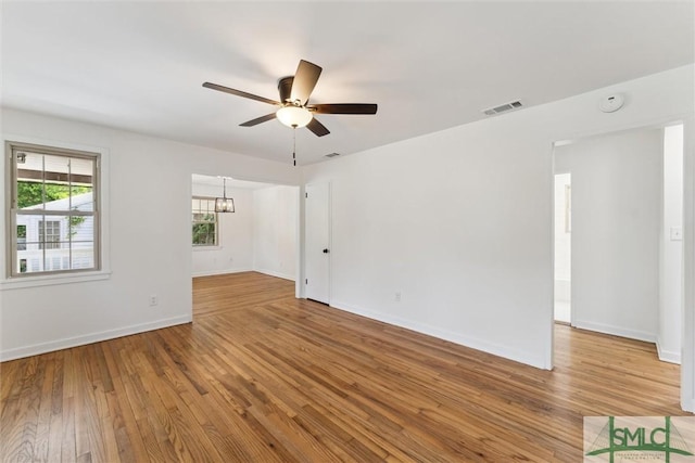 unfurnished room featuring baseboards, ceiling fan with notable chandelier, wood finished floors, and visible vents