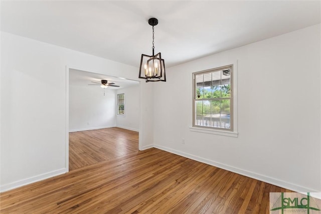 unfurnished dining area with light wood-type flooring, baseboards, ceiling fan with notable chandelier, and a healthy amount of sunlight
