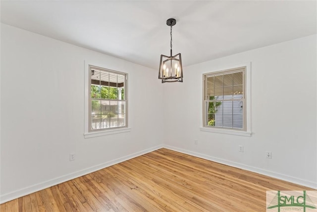 empty room with an inviting chandelier, light wood-style floors, and baseboards
