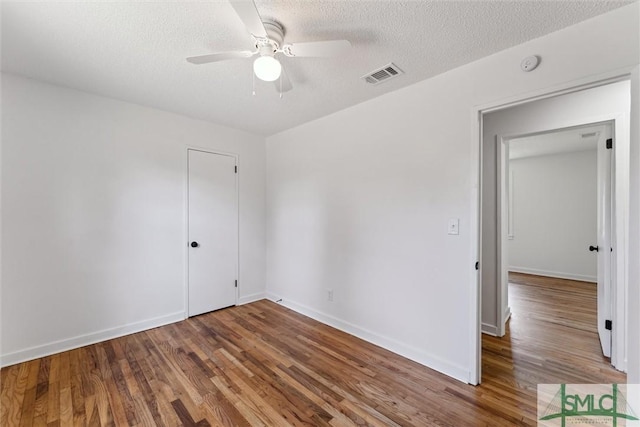 empty room with ceiling fan, a textured ceiling, baseboards, wood finished floors, and visible vents