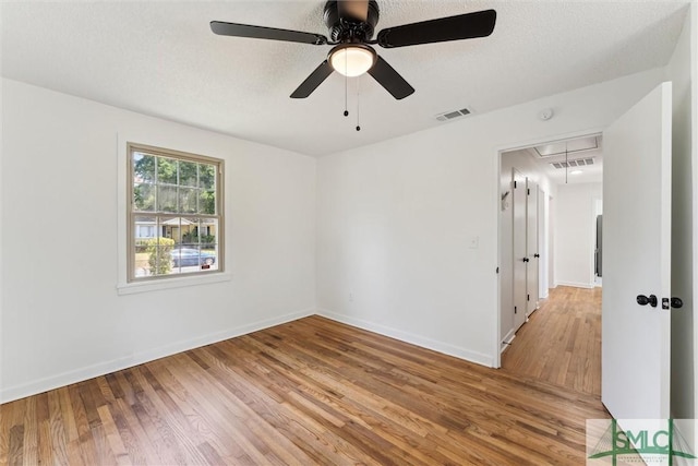 empty room featuring a ceiling fan, visible vents, attic access, and light wood-style floors