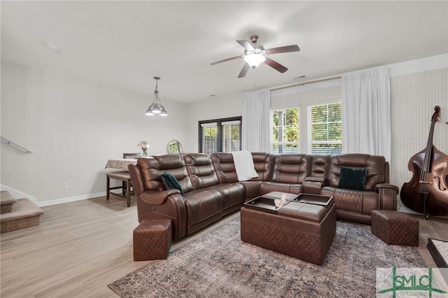 living area featuring baseboards, ceiling fan, wood finished floors, and stairway