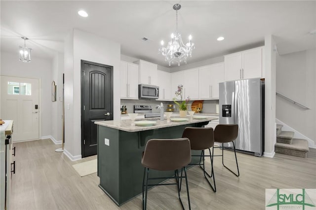 kitchen with an inviting chandelier, light wood-style floors, a center island with sink, white cabinetry, and stainless steel appliances