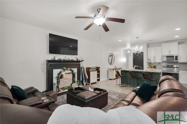 living room with baseboards, light wood finished floors, ceiling fan with notable chandelier, and recessed lighting