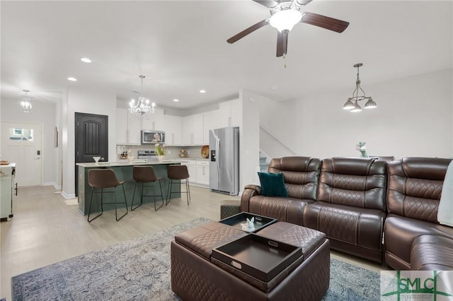 living room featuring recessed lighting, baseboards, light wood finished floors, and ceiling fan with notable chandelier