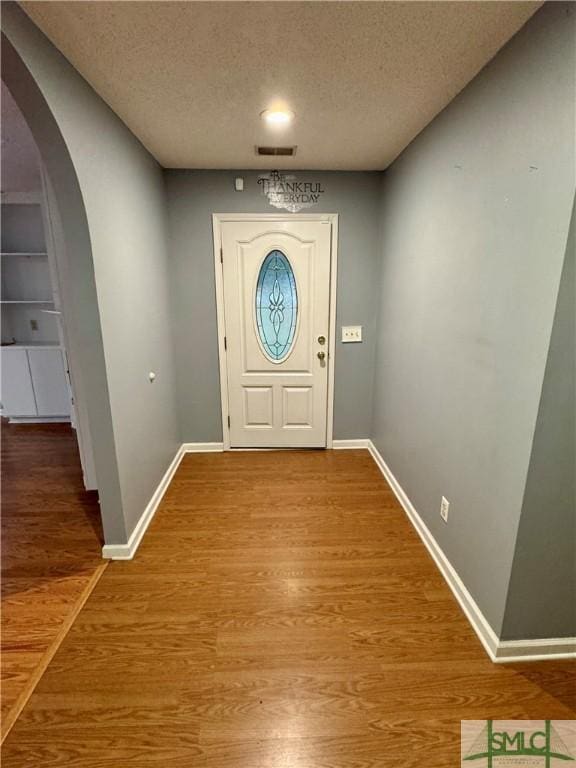 foyer entrance with arched walkways, a textured ceiling, visible vents, and wood finished floors
