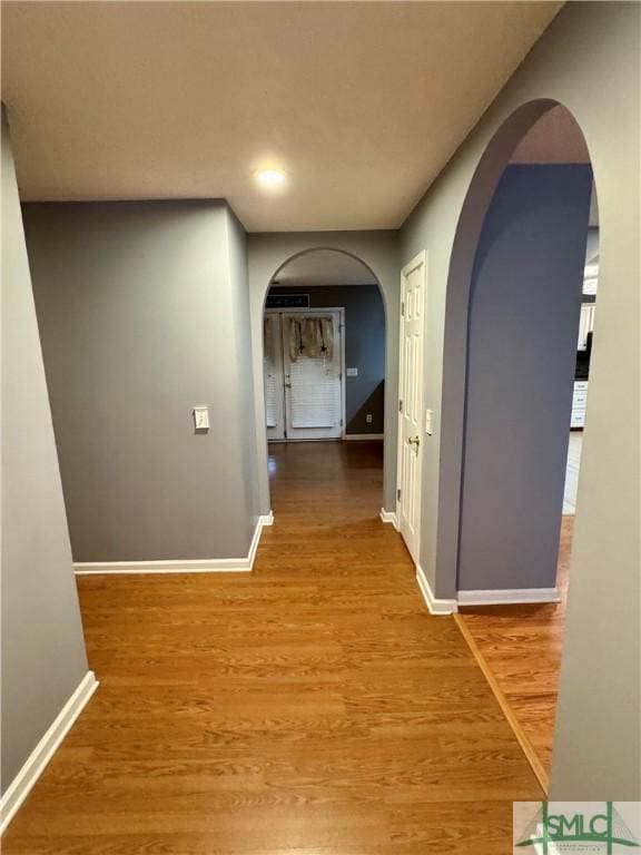 hallway featuring arched walkways, baseboards, recessed lighting, and wood finished floors