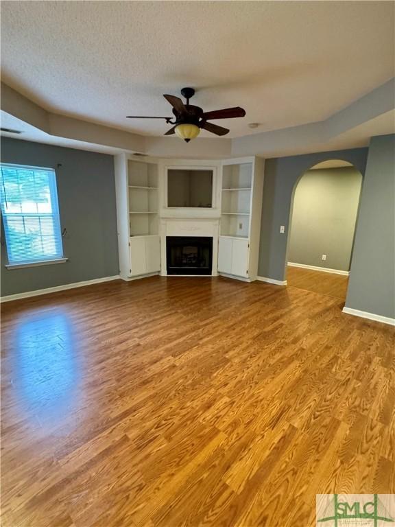 unfurnished living room featuring a ceiling fan, a textured ceiling, arched walkways, a fireplace, and baseboards