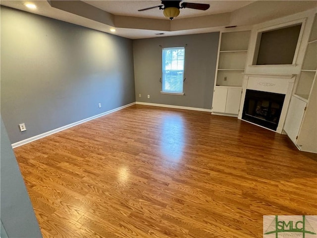 unfurnished living room featuring baseboards, ceiling fan, wood finished floors, and built in shelves