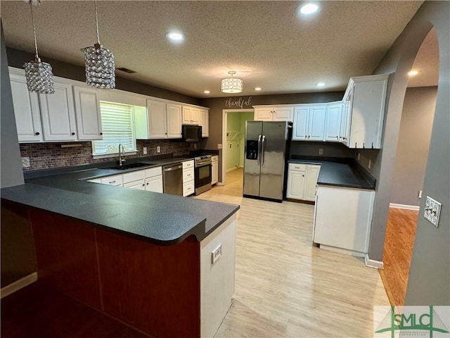 kitchen with dark countertops, a textured ceiling, a sink, light wood finished floors, and stainless steel appliances