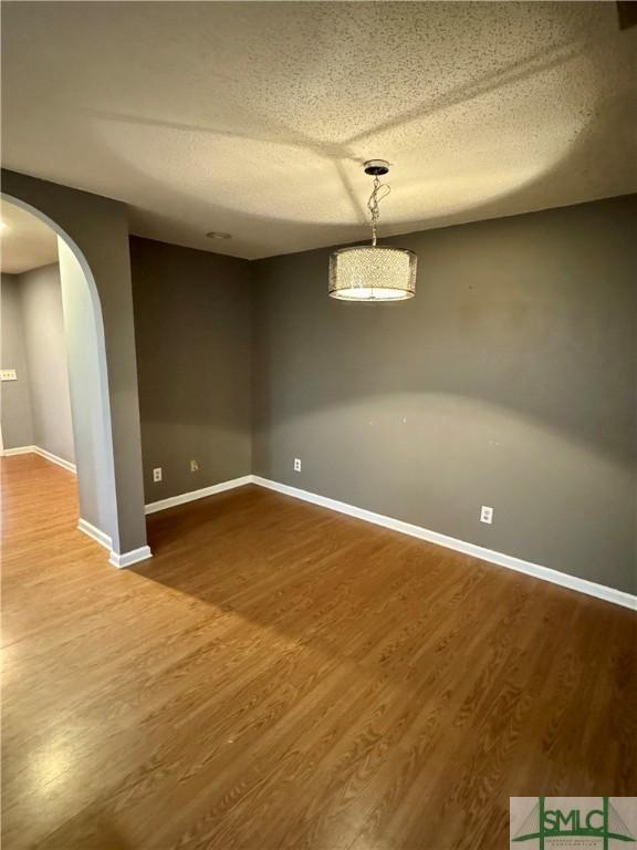 unfurnished room featuring arched walkways, baseboards, a textured ceiling, and wood finished floors