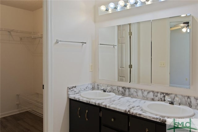 full bath featuring double vanity, a spacious closet, a sink, and wood finished floors