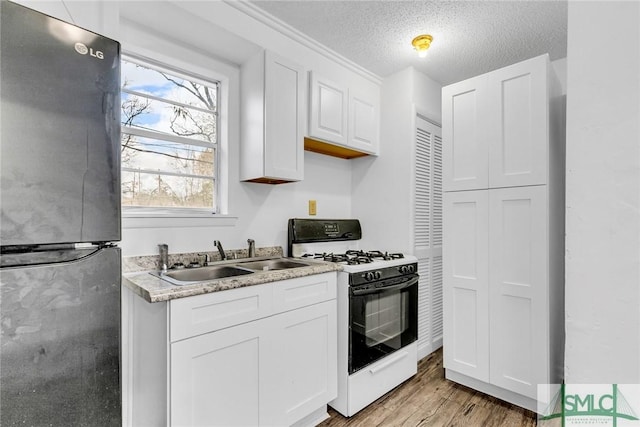 819 W 51st St, Savannah, GA 31405 - kitchen featuring freestanding refrigerator, gas range, a sink, white cabinetry, and a textured ceiling