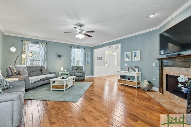 living area with ceiling fan, a fireplace, a textured ceiling, light wood-type flooring, and ornamental molding