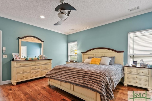 bedroom featuring ceiling fan, a textured ceiling, visible vents, wood finished floors, and ornamental molding
