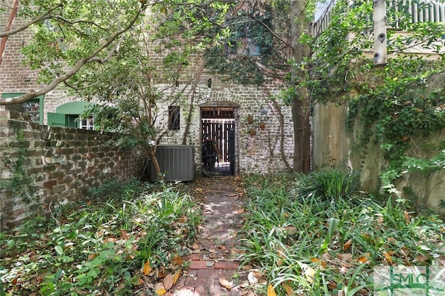 doorway to property with central AC, brick siding, and fence
