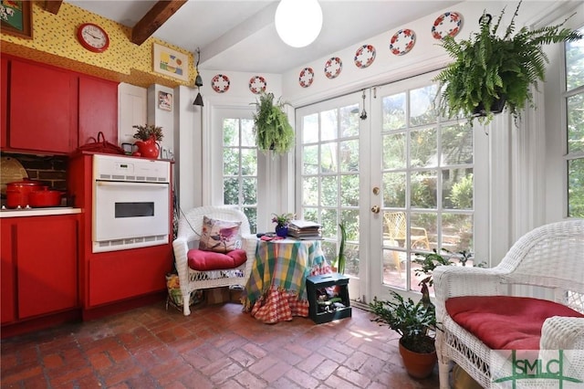 sunroom / solarium with french doors, beam ceiling, and brick floor