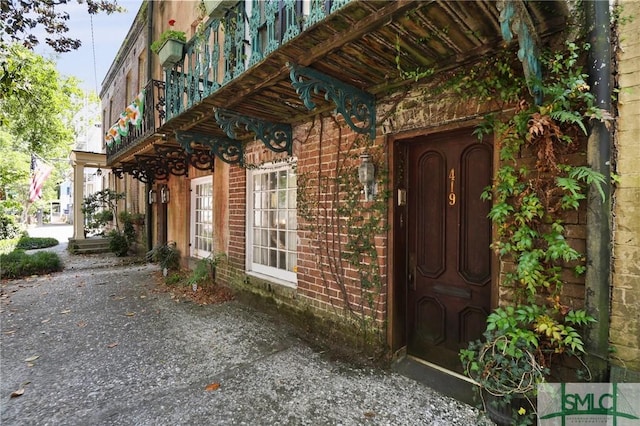 view of exterior entry with a balcony and brick siding
