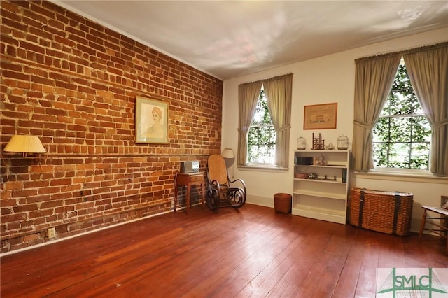 sitting room with brick wall and hardwood / wood-style flooring