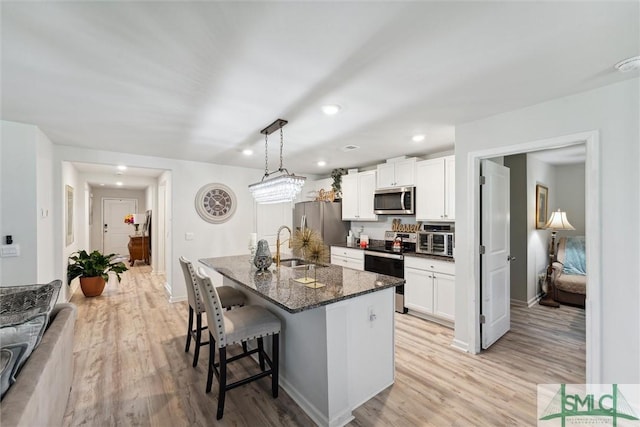 kitchen with white cabinetry, stainless steel appliances, a breakfast bar area, and light wood-type flooring