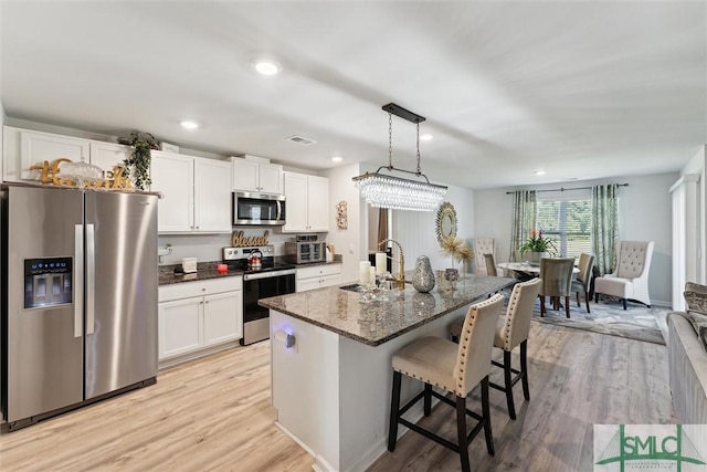 kitchen with a sink, a kitchen breakfast bar, white cabinets, light wood-type flooring, and appliances with stainless steel finishes