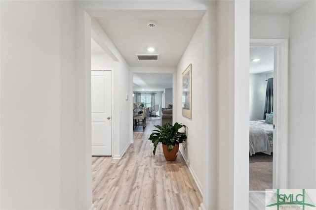 corridor with visible vents, light wood-style flooring, and baseboards
