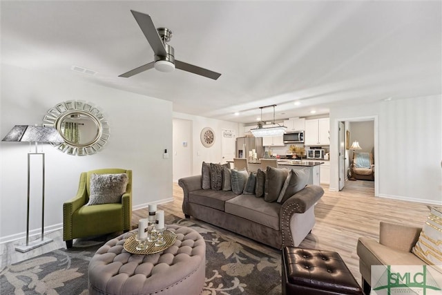 living room featuring baseboards, a ceiling fan, and light wood-style floors