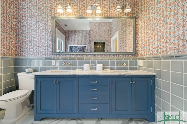 bathroom featuring tile walls, wainscoting, wallpapered walls, and a sink