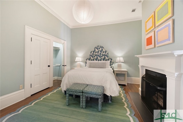 bedroom featuring wood finished floors, visible vents, a fireplace, crown molding, and baseboards