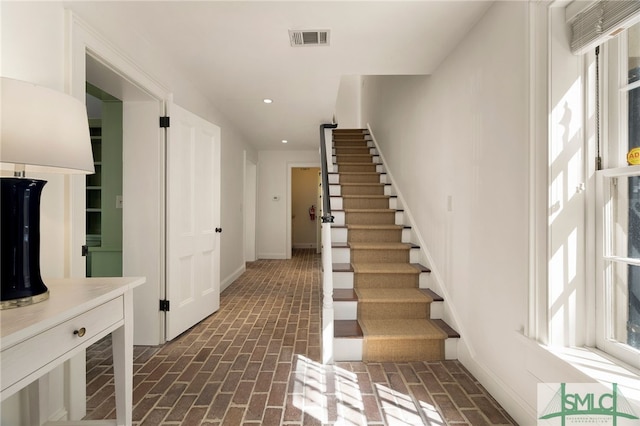 stairway featuring visible vents, brick floor, and recessed lighting