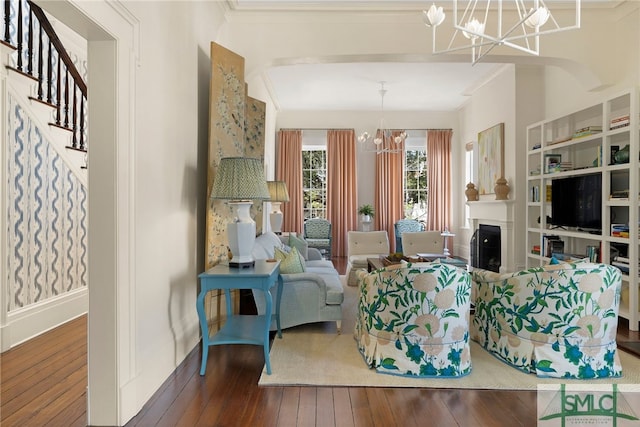 living room featuring wood-type flooring, a fireplace, stairway, a chandelier, and ornamental molding