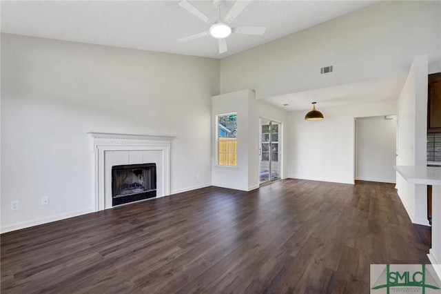 unfurnished living room with dark wood-type flooring, visible vents, a fireplace, ceiling fan, and baseboards