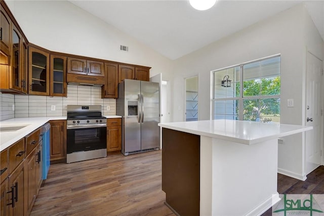 kitchen with stainless steel appliances, wood finished floors, visible vents, vaulted ceiling, and backsplash