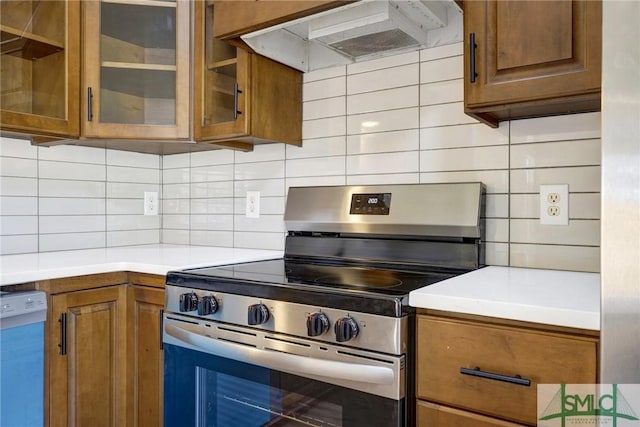 kitchen featuring brown cabinetry, stainless steel electric range, dishwashing machine, ventilation hood, and backsplash