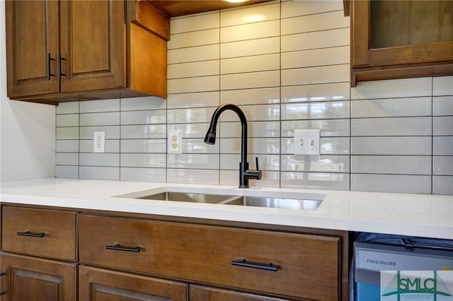 kitchen featuring dishwashing machine, decorative backsplash, a sink, and brown cabinets