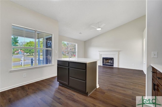 kitchen with a ceiling fan, lofted ceiling, dark wood-style flooring, light countertops, and a fireplace